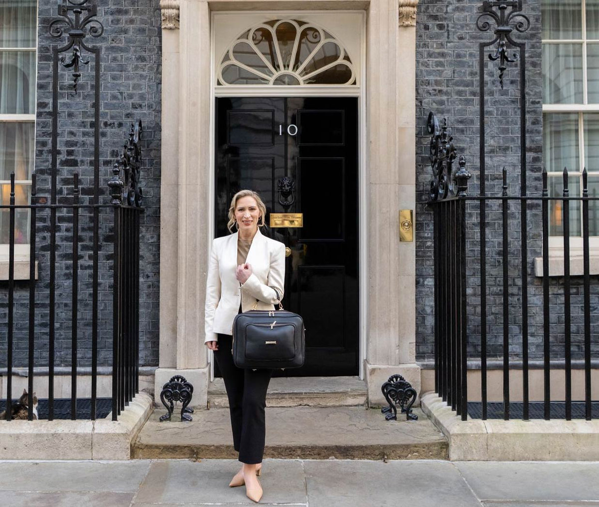 Woman holding a AVAIA Noir in front of a number 10 Downing Street.