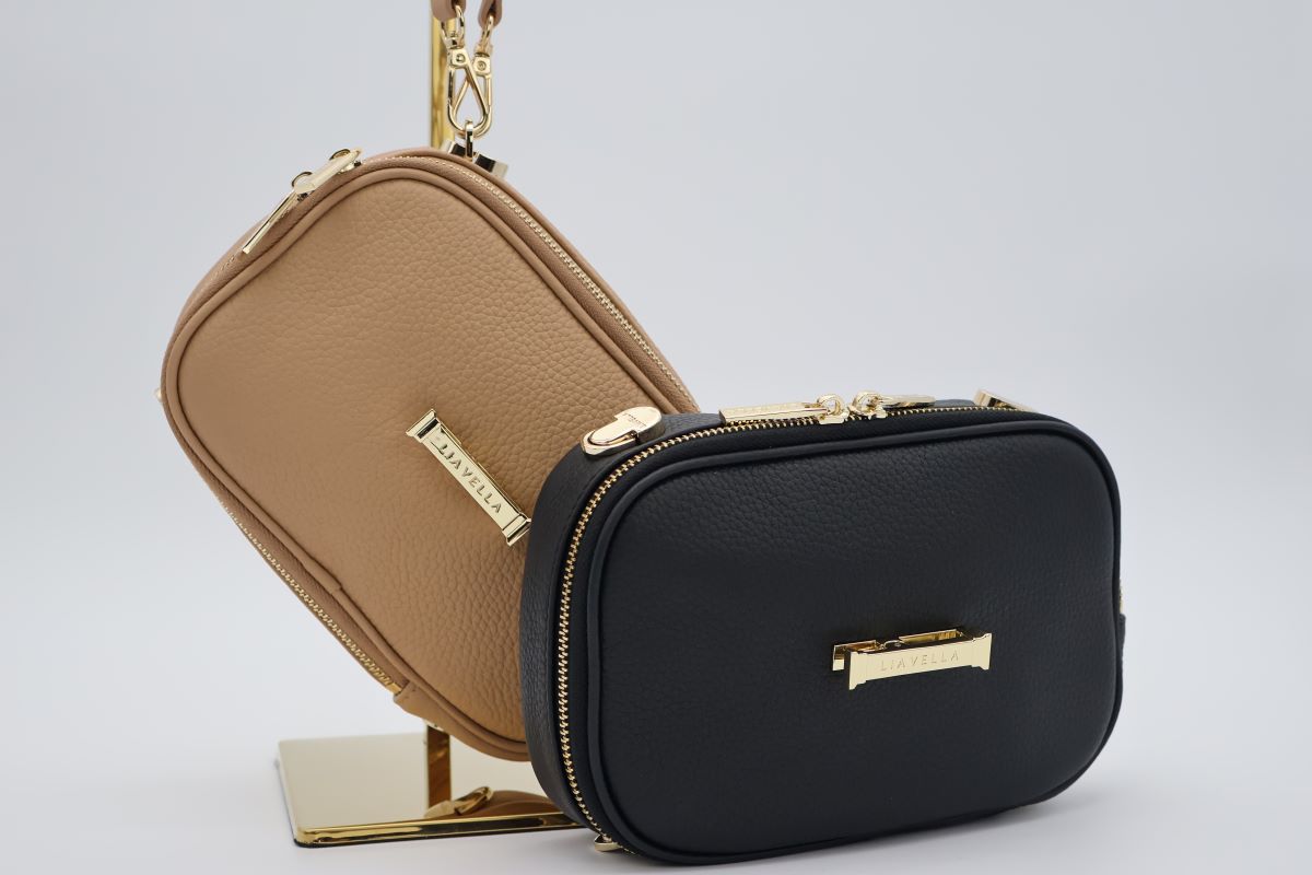 Two AVAIA Petit bags in two different colours, one resting on a gold holder, against a grey background.