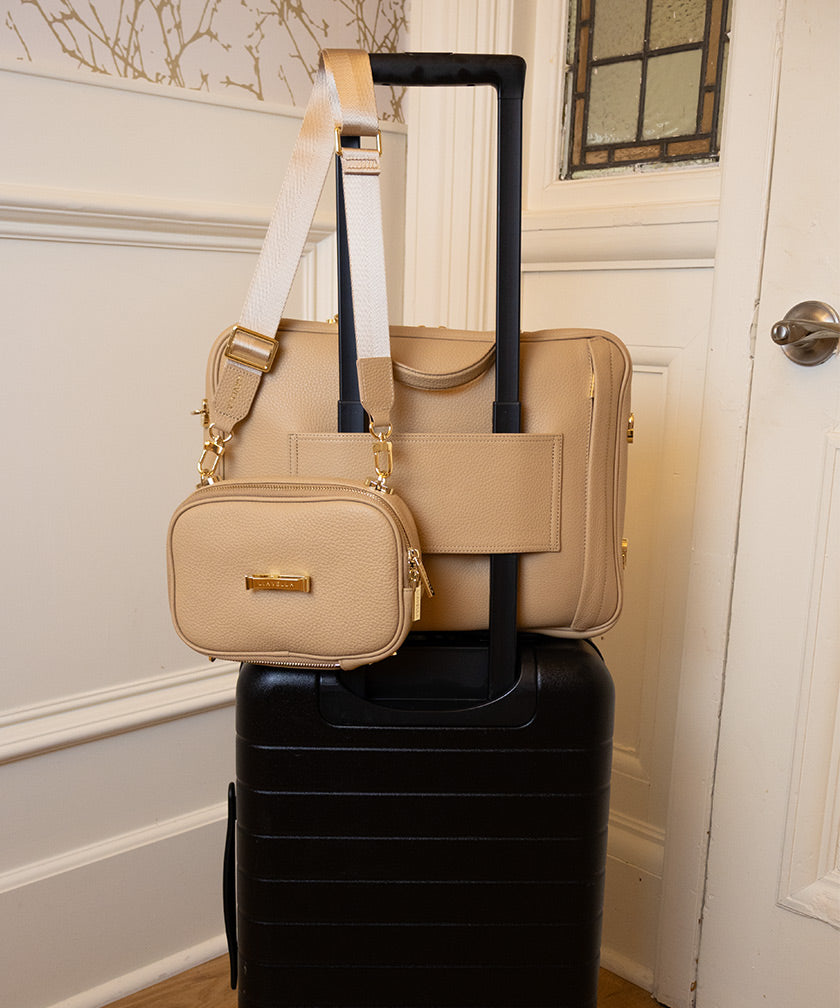 The leather bags AVAIA crème caramel on suitcase using pass-through strap and the AVAIA Petit crème caramel held by suitcase handles.