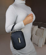Load image into Gallery viewer, The AVAIA Petit bag worn over the arm with the handheld leather strap by a woman wearing a grey ribbed sweater.