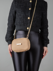 A person wearing a crème caramel AVAIA Petit as a crossbody bag, using a long gold chain strap.