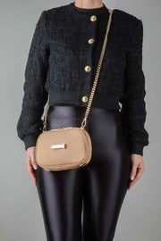A person wearing a black outfit and a crème caramel AVAIA Petit as a crossbody bag, using a padded chain gold strap.