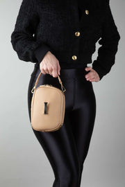 A person in a black outfit, holding a crème caramel AVAIA Petit, using a leather handheld strap.