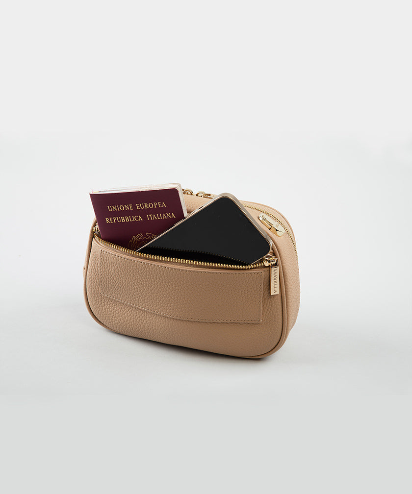 The back pocket of a crème caramel AVAIA Petit bag, with a phone and passport inside, on a studio background.