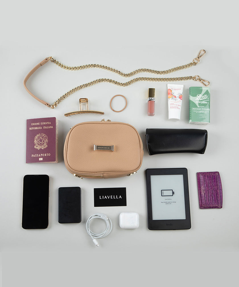 Collection of travel items including a crème caramel AVAIA Petit bag, phone, passport, and e-reader on a light gray background.