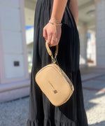 Load image into Gallery viewer, Person holding a crème caramel AVAIA Petit, using the handheld strap as a wristlet, with a blurred background