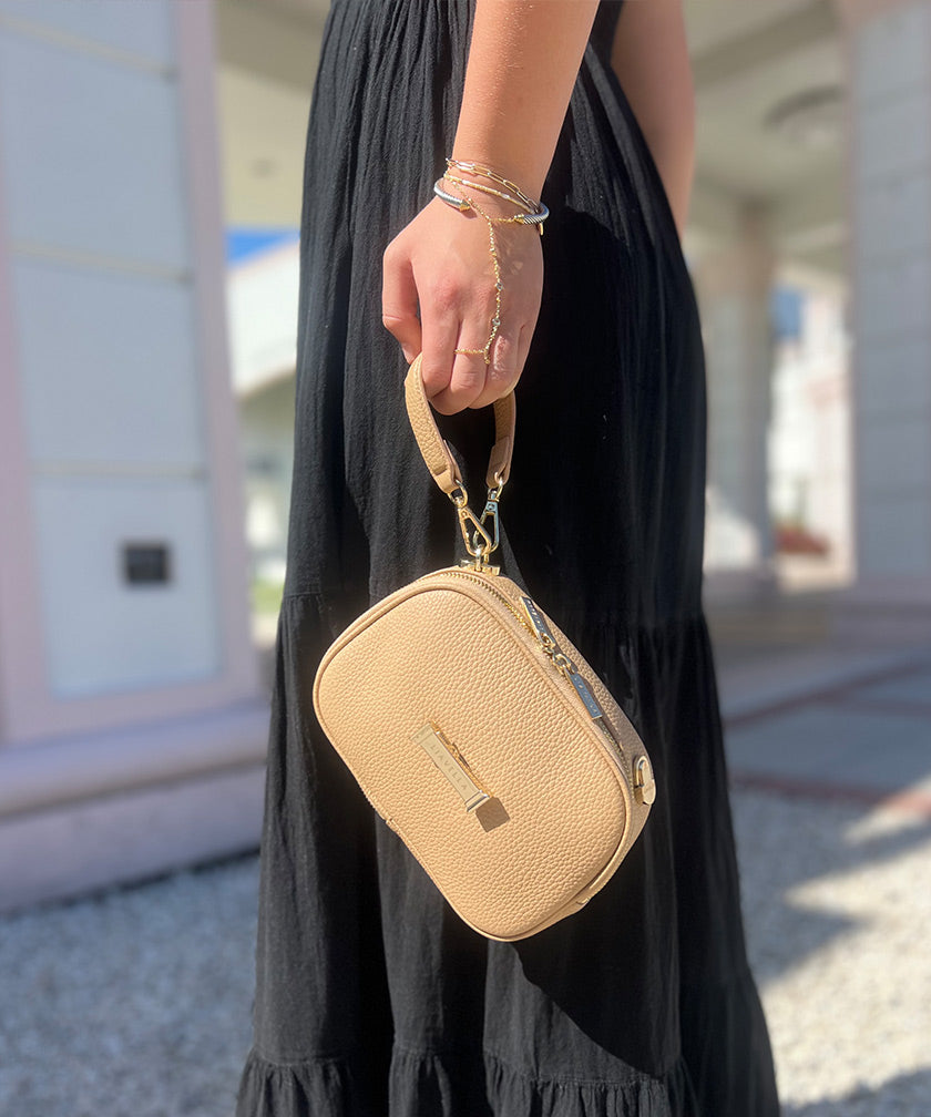 Person holding a crème caramel AVAIA Petit, using the handheld strap as a wristlet, with a blurred background