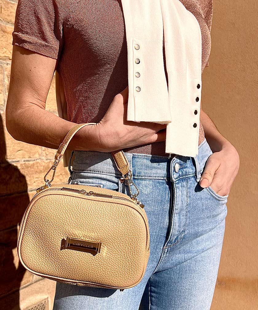 Person holding a AVAIA Petit in crème caramel, using a handheld strap.