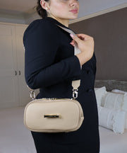 Woman holding a AVAIA Petit creme caramel bag, as a shoulder bag, using a fabric strap. 