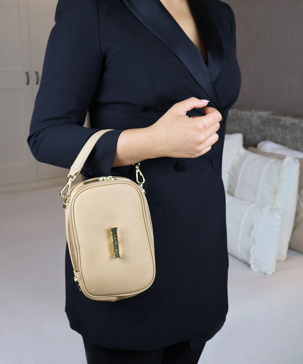 Woman in a dark blazer wearing the AVAIA Petit as a wristlet bag, in an indoor setting.