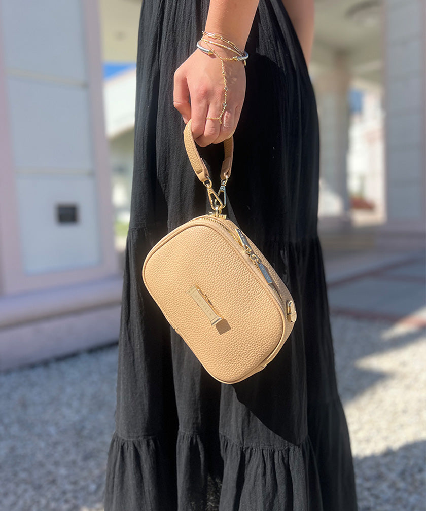 A person holding a crème caramel AVAIA Petit bag using the handheld strap in the wristlet style.