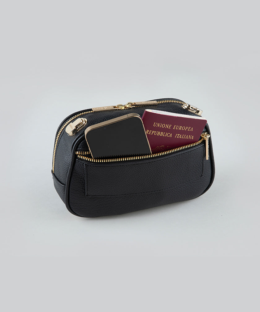 The back pocket of a noir AVAIA Petit bag, with a phone and passport inside, on a studio background.