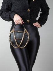 A person holding a AVAIA Petit noir bag, using the long chain strap twisted into a handheld style.