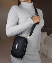 A woman in a grey sweater wearing an AVAIA Petit as a crossbody bag in an indoor setting.