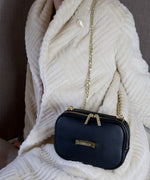 Load image into Gallery viewer, A person wearing white fur coat and a noir AVAIA Petit as a shoulder bag, using the padded gold chain strap.