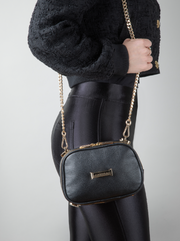 A person wearing a noir AVAIA Petit as a shoulder bag, using the long gold chain strap.