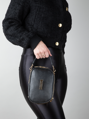 A person holding a AVAIA Petit noir bag in the vertical orientation, using the handheld leather strap.