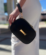 Load image into Gallery viewer, A person holding a noir AVAIA Petit using the leather handheld strap, wearing it in the wristlet style.