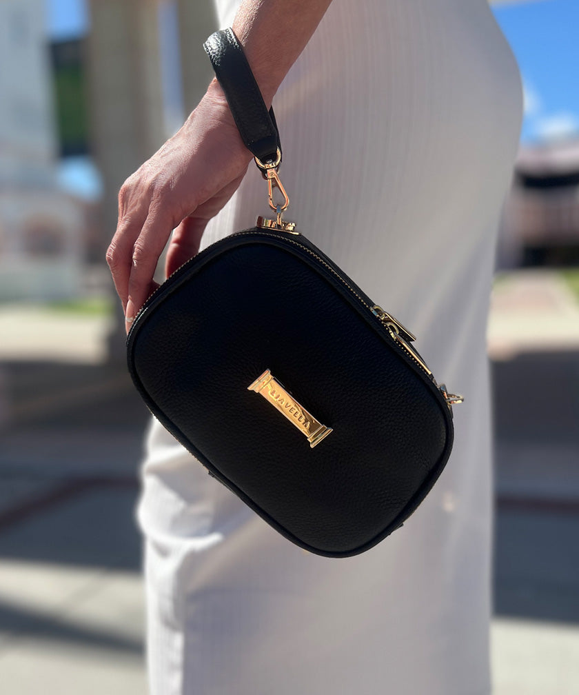 A person holding a noir AVAIA Petit using the leather handheld strap, wearing it in the wristlet style.