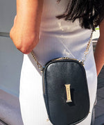 Load image into Gallery viewer, A close up shot of the AVAIA Petit in noir, highlighting the gold sunglass clip with the LIAVELLA branding on it.