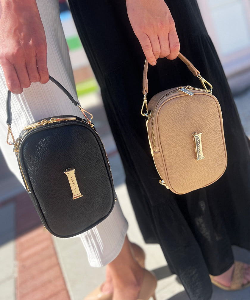 Two AVAIA Petit bags, one in crème caramel and one in noir, both with the handheld strap, in vertical orientation.