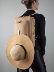 Person wearing a AVAIA backpack in creme caramel with a straw hat attached, on a plain background