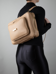 A person wearing a crème caramel AVAIA as a backpack, using two long leather straps.