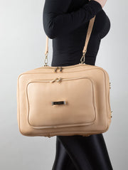 A person wearing a crème caramel AVAIA as a shoulder bag, using the long leather strap, in a studio.