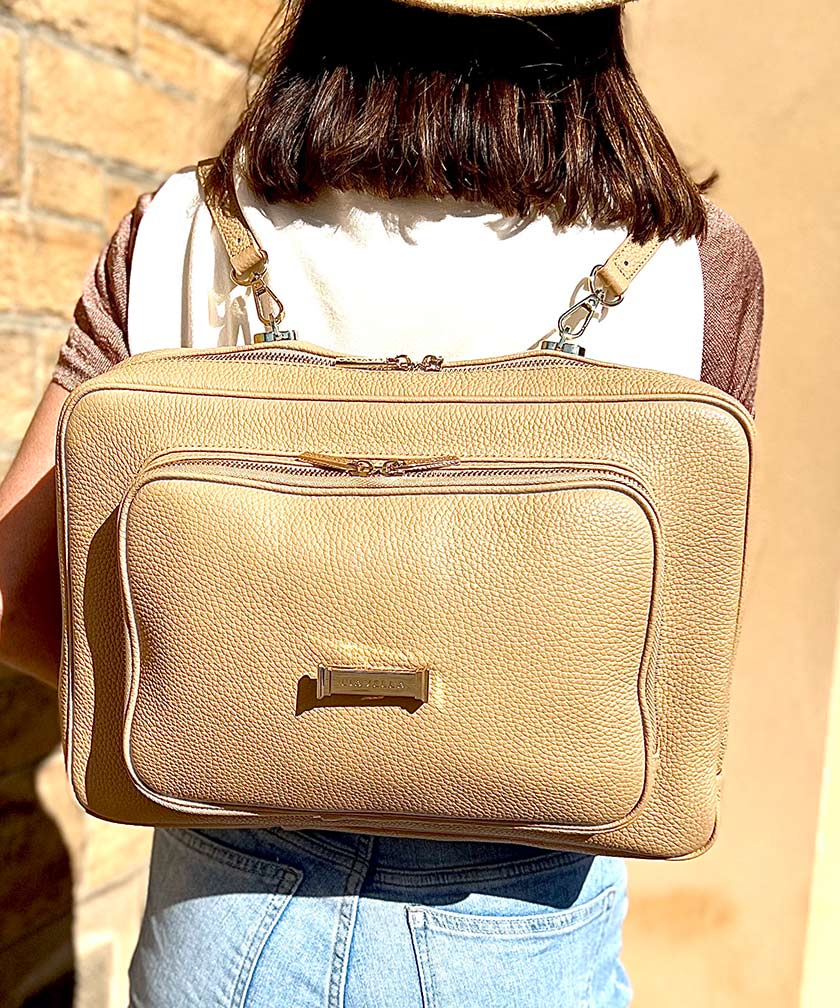 A person wearing a crème caramel AVAIA as a backpack, using two long leather straps.