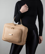 Load image into Gallery viewer, Person holding a crème caramel AVAIA bag, in horizontal orientation, using the handheld strap.