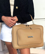 Load image into Gallery viewer, Crème caramel AVAIA bag with the handheld strap, held by a person wearing a black jacket and white skirt.