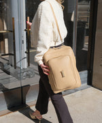 Load image into Gallery viewer, A person wearing a crème caramel AVAIA as a shoulder bag, using a longer leather strap, walking into a building.