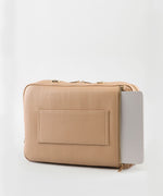 Load image into Gallery viewer, A crème caramel AVAIA bag, with a laptop in its padded back pocket, on a studio background.