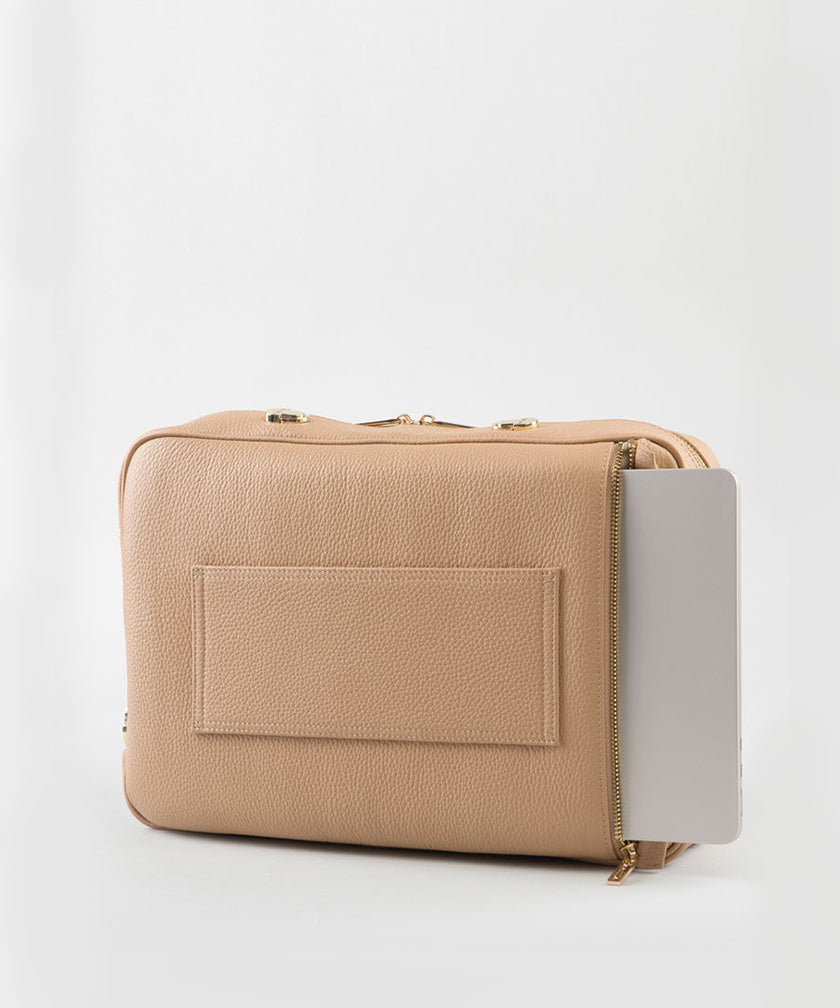 A crème caramel AVAIA bag, with a laptop in its padded back pocket, on a studio background.