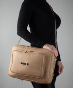 Load image into Gallery viewer, Person wearing the AVAIA crème caramel as a crossbody bag, using a padded chain gold strap, against a gray background