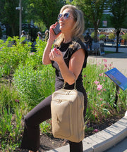 Woman talking on a phone with a crème caramel AVAIA bag, using a handheld strap, in an outdoor setting.