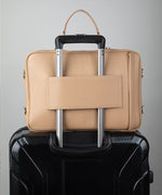 Load image into Gallery viewer, Crème caramel AVAIA bag, using the luggage pass through strap, placed on a black suitcase.