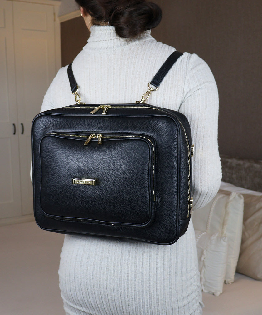 A woman wearing the AVAIA bag as a horizontal backpack, she is wearing a grey ribbed sweater indoors.
