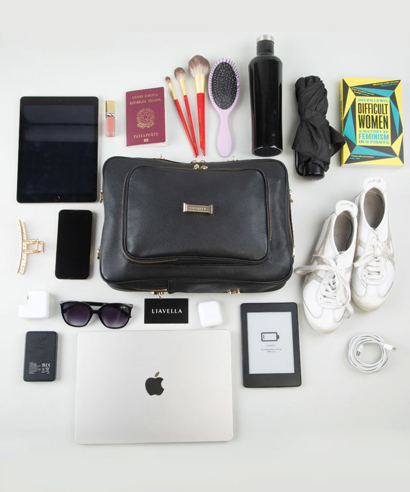 Collection of travel items including a black AVAIA bag, tablet, phone, laptop, and various personal items on a white background.
