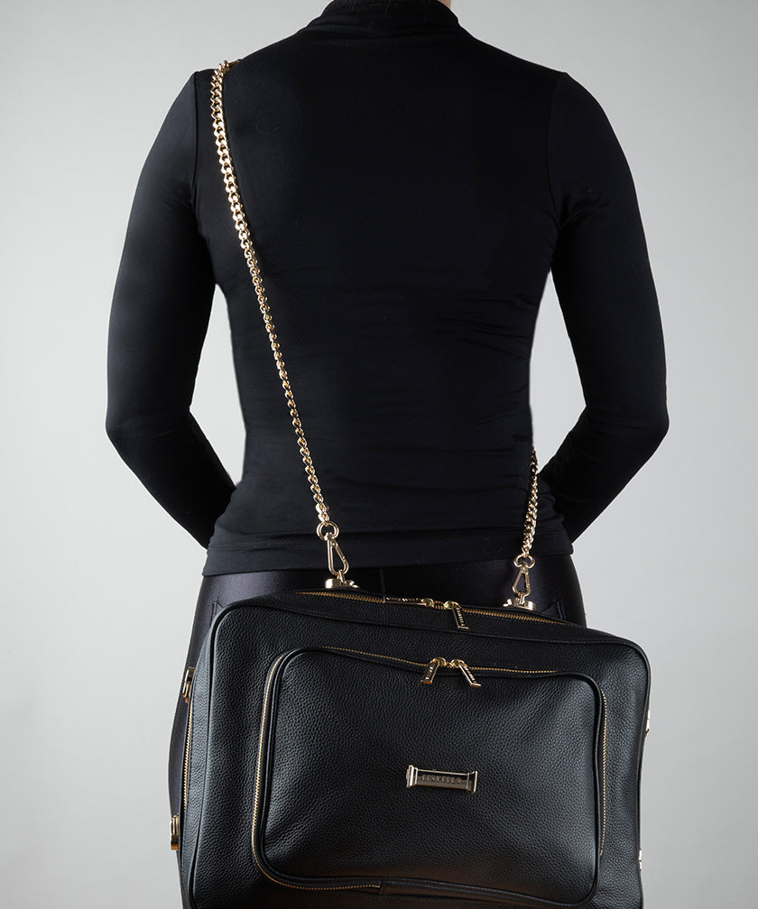 Person wearing an AVAIA bag in noir as a crossbody, using a padded chain strap on a gray background