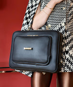 Load image into Gallery viewer, A person holding an AVAIA Noir bag, using a handheld strap, on a red background.