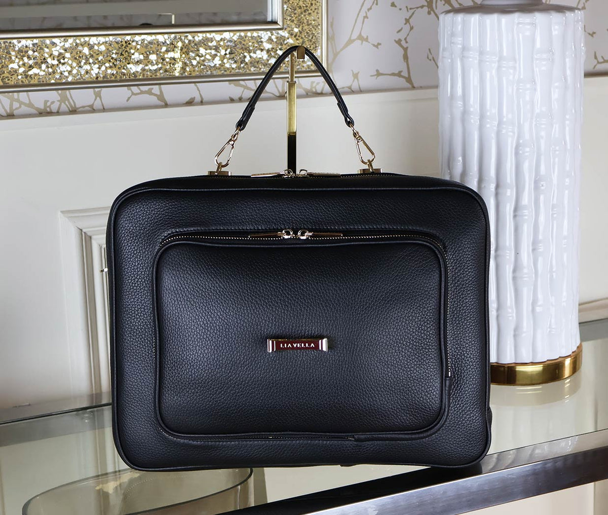 The AVAIA Noir a black leather handbag on a reflective surface with decorative background