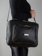 A person wearing a noir AVAIA bag as a shoulder bag, using a long leather strap, in a studio.