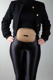 A person wearing a black outfit wearing a crème caramel AVAIA Petit as a bumbag around their waist, using the fabric strap.