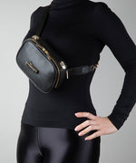 Load image into Gallery viewer, Person wearing a black outfit with a black leather bag, the AVAIA Petit, worn crossbody on a gray background