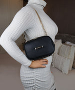 Load image into Gallery viewer, The AVAIA Petit bag in horizontal position being worn over the shoulder with a gold chain strap by a woman in a grey ribbed sweater.