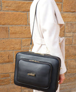 Load image into Gallery viewer, A person in a white coat, wearing the AVAIA bag over the shoulder against a brickwall backdrop.
