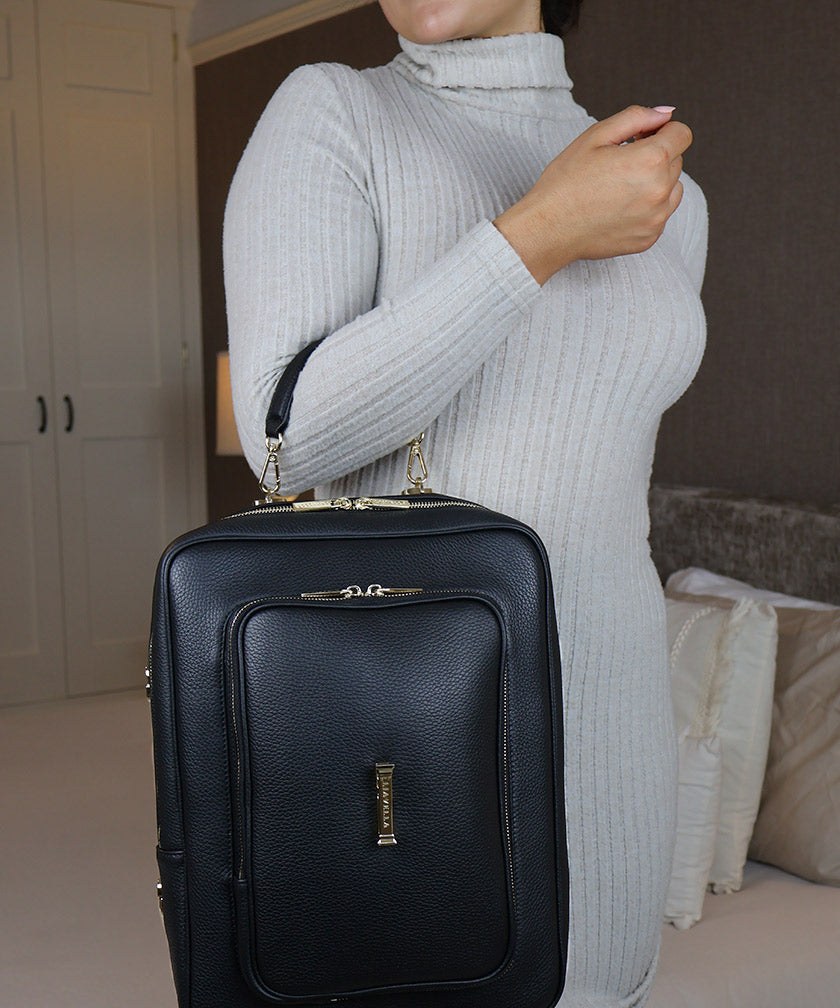 Woman holding the AVAIA bag using the handheld leather strap, she is indoors.