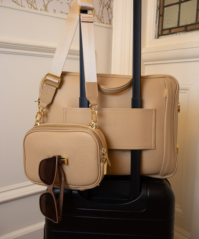 AVAIA crème caramel leather bag on suitcase using pass-through strap with AVAIA Petit crème caramel handbag on handle holding sunglasses.