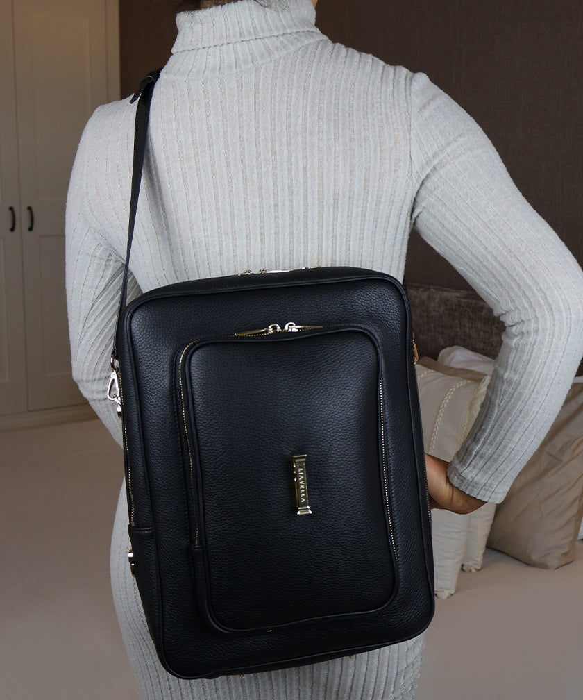 Woman in a grey jumper wearing the AVAIA bag in Noir as a crossbody bag in vertical position.